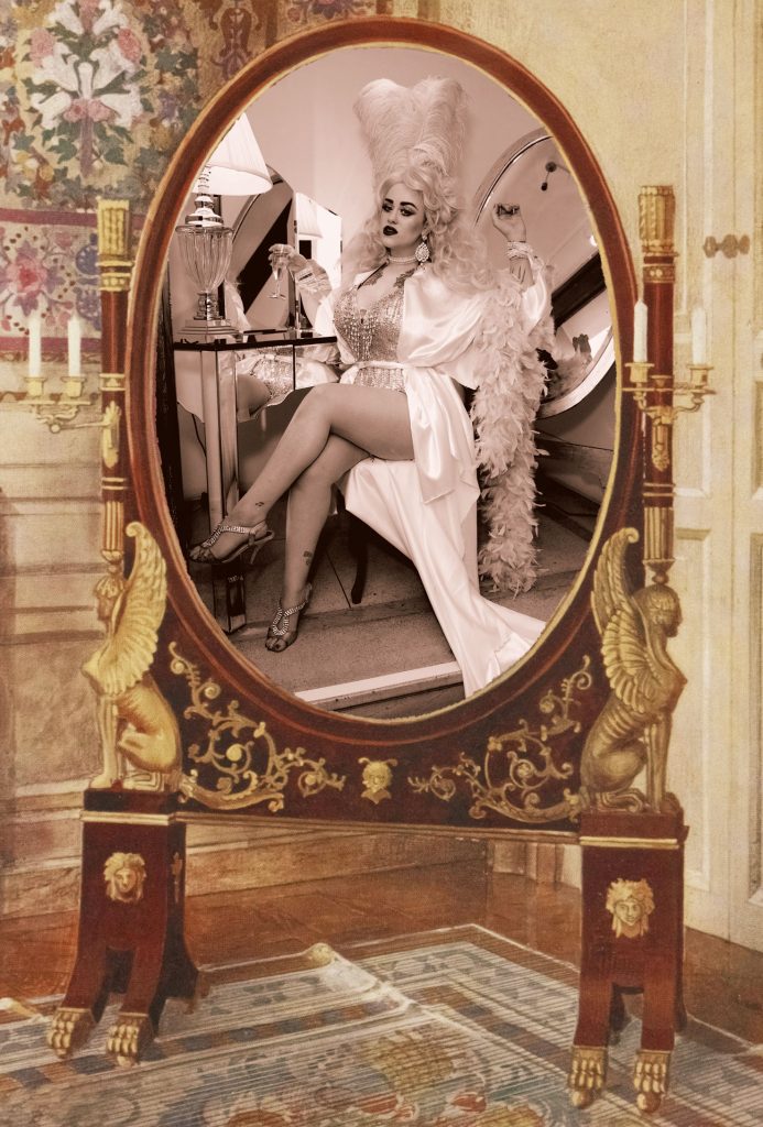 A woman seen in an oval mirror with a large white wig on.
