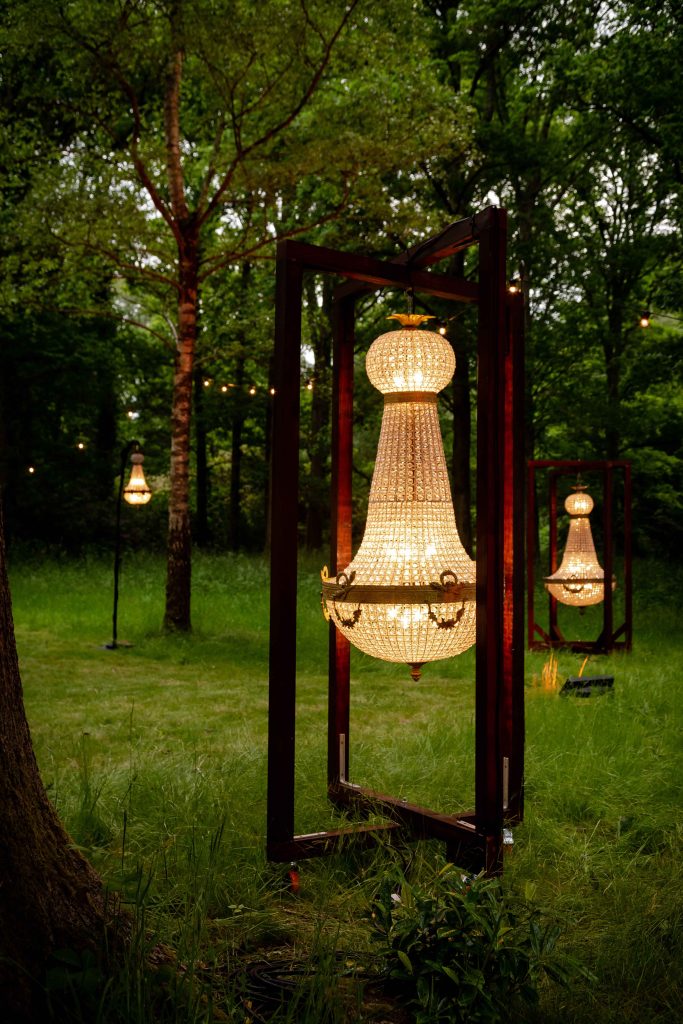 Three large crystal chandelier in a bespoke wooden cross frame set on a green lawn in a woodlands