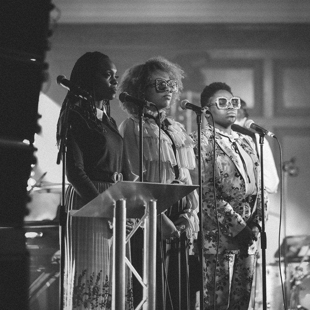 Black and white image of three singers on stage with microphones.
