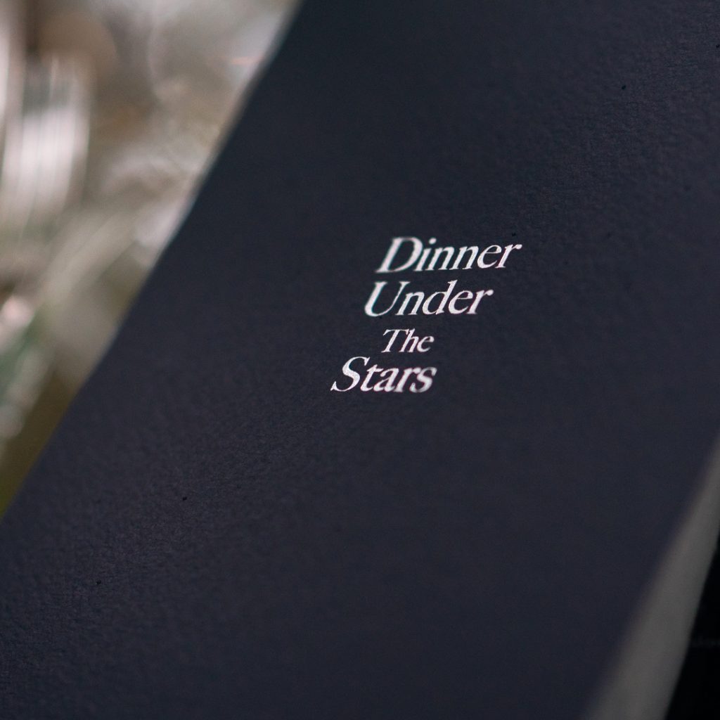 A midnight blue menu with silver foiling typography that reads 'Dinner Under the Stars' on the front