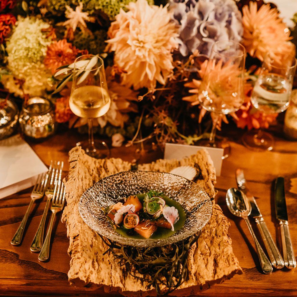 A circular glass bowl of food containing seafood set on a piece of wood as a place-setting.