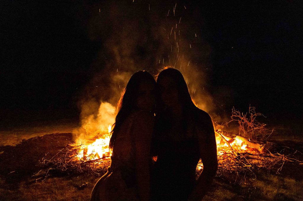Two figures huggings in front of a glowing bonfire