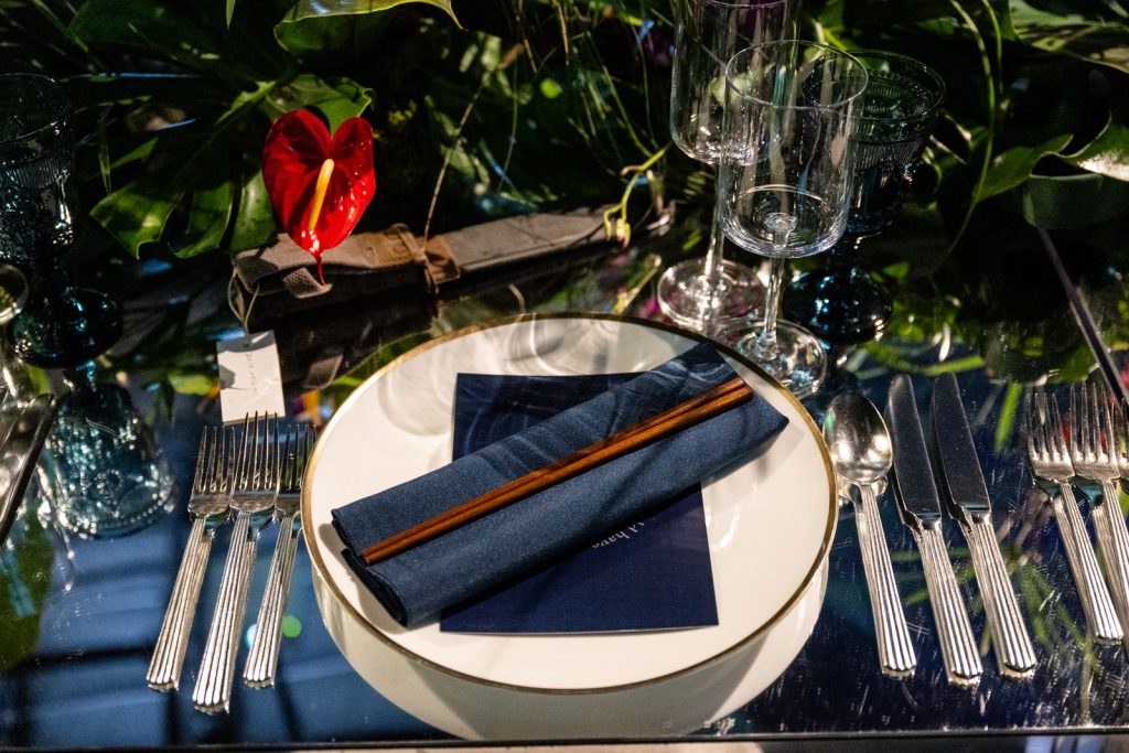 A dinner place setup of flatware and china including midnight blue napkin and chopsticks.