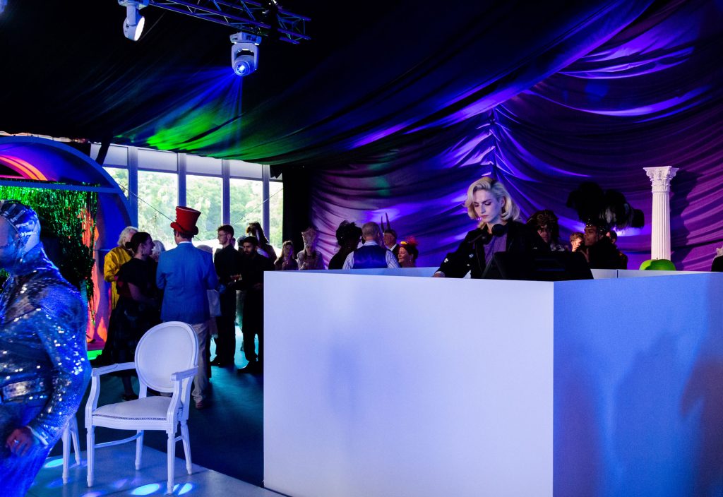 A DJ in a white DJ booth and a white chair on a dance floor.