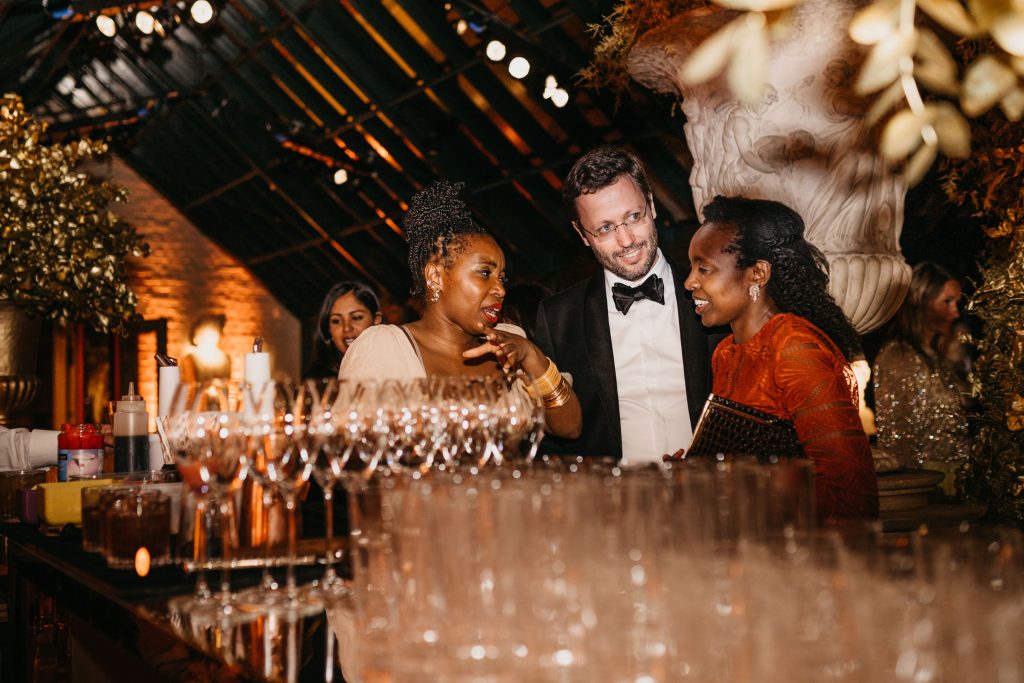 Three people at a bar with masses of glassware.