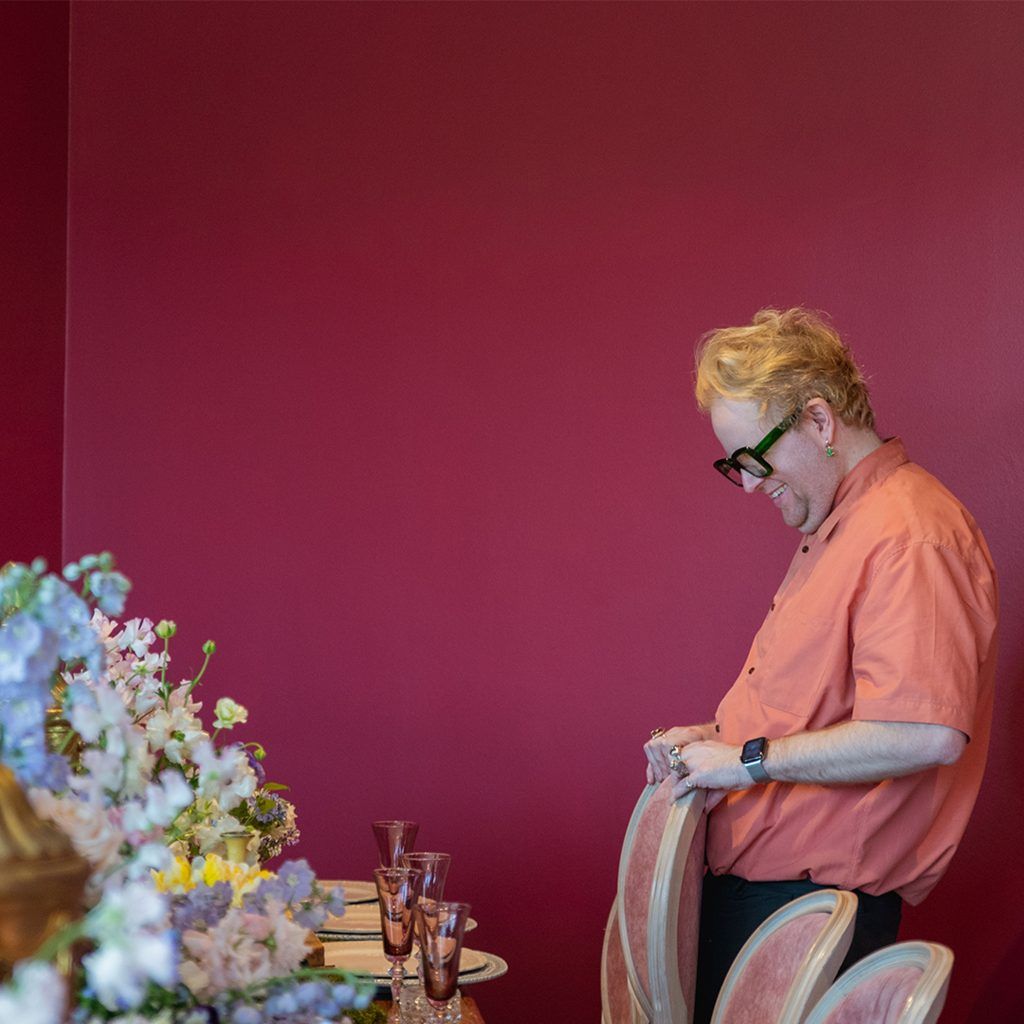 A man wearing an orange shirt pushing in a dining chair