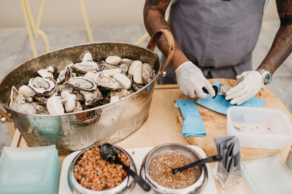 An oyster shucker opening oyster and oysters on display in a large silver container