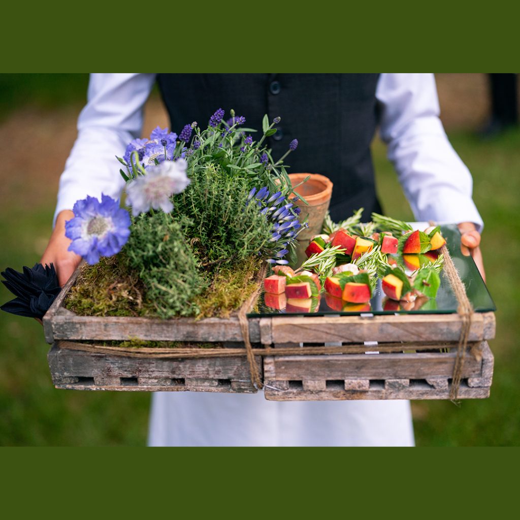 A person holding a tray of canapés which is dressed with herbs