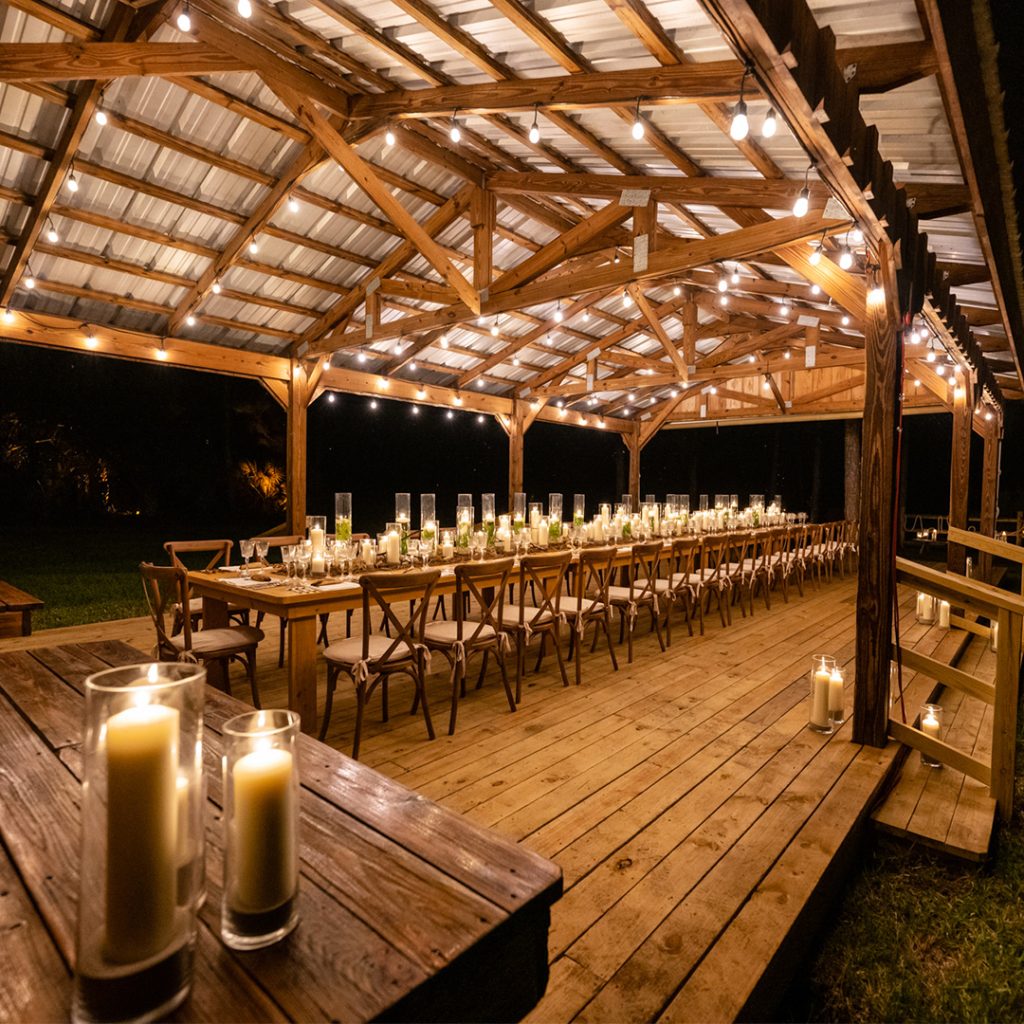 Long wooden table under a wooden veranda dressed with tonnes of lit candles.