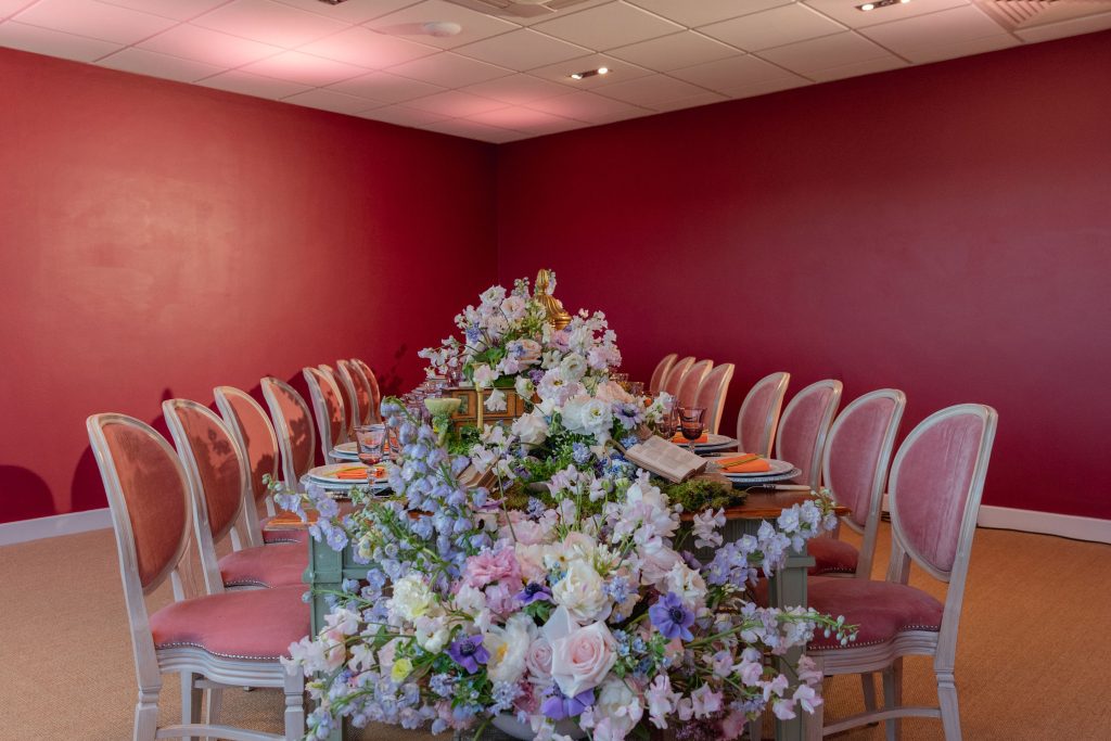 A dining room setup with pink chairs and a large runner of spring pastel coloured flowers in various styles