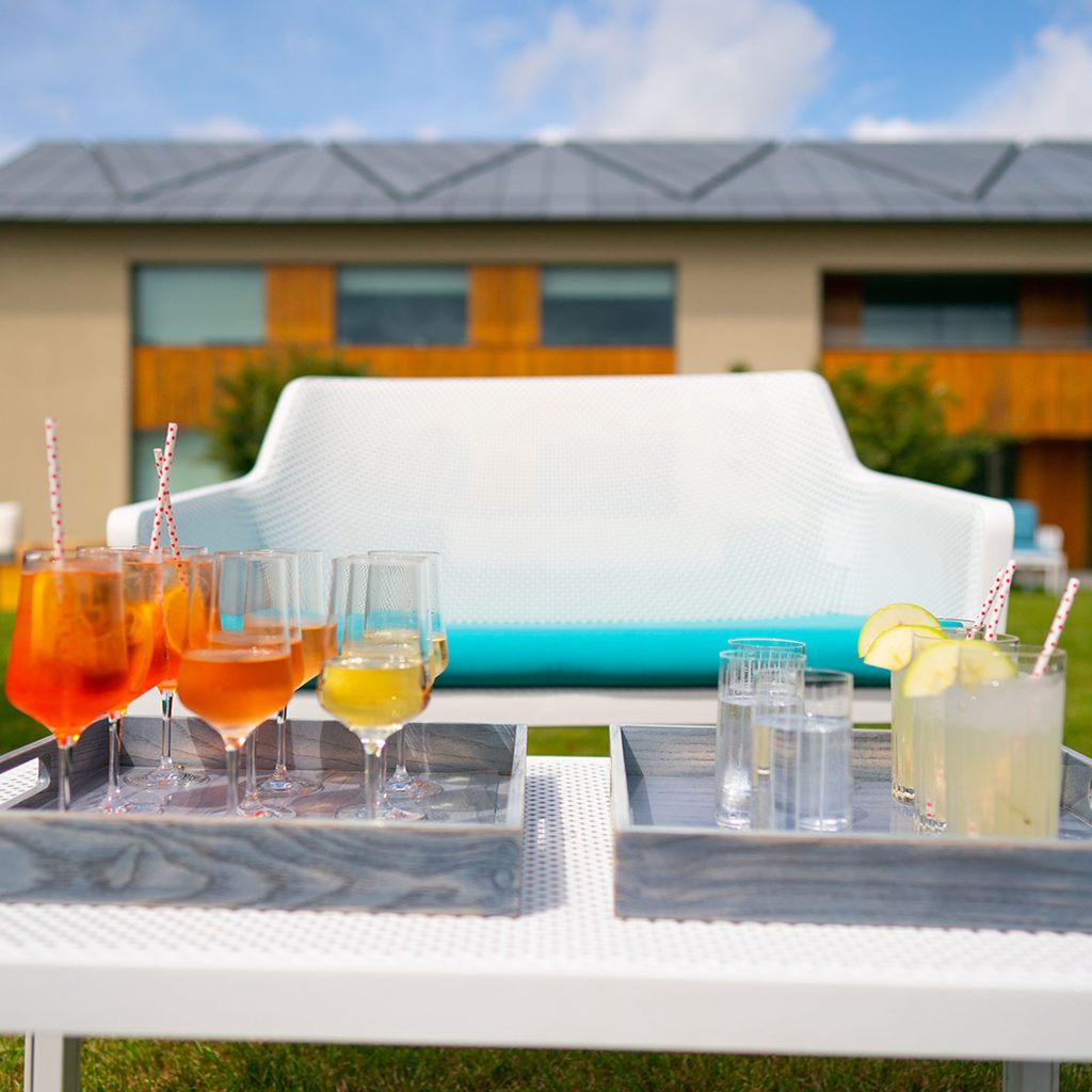 White chair with blue cushion behind a white table laid with glasses filled with various coloured liquids