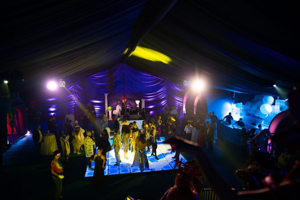 People on a dance floor in a marquee draped and lit in purple.