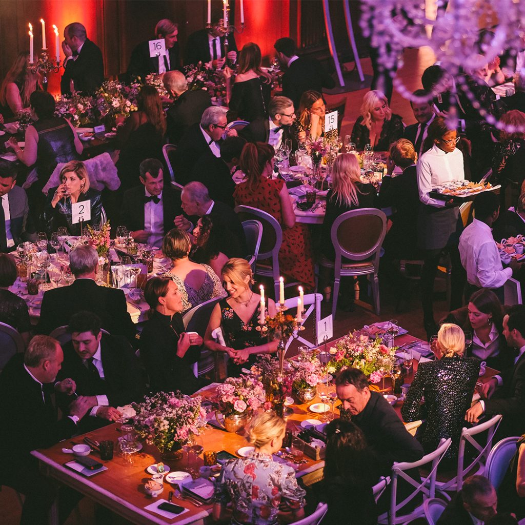 A room filled with dining tables and chairs with people sat at these tables and chairs eating dinner.