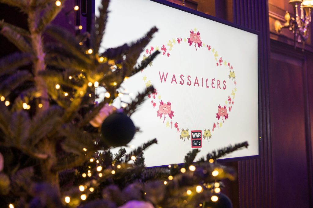 A screen showing a graphic with a border that says "Wassailers" behind a Christmas tree lit with fairy lights.