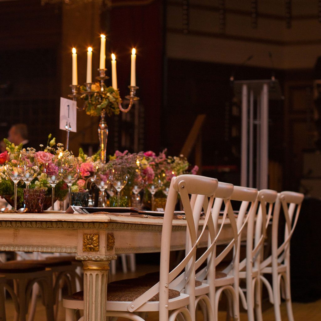A white dining table with white cross-back chairs dressed with flowers and a glowing, lit candelabra.