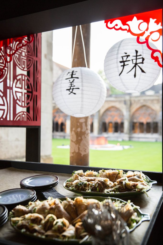 Asian style food presented on large platters beneath two white round paper lanterns.