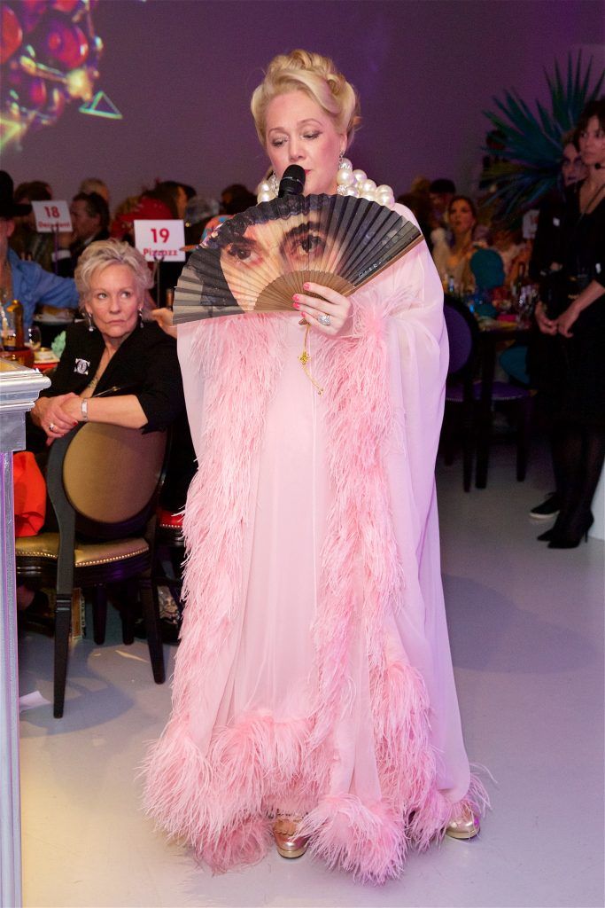 Woman in a pink dress holding a fan with a painted face on the outside.