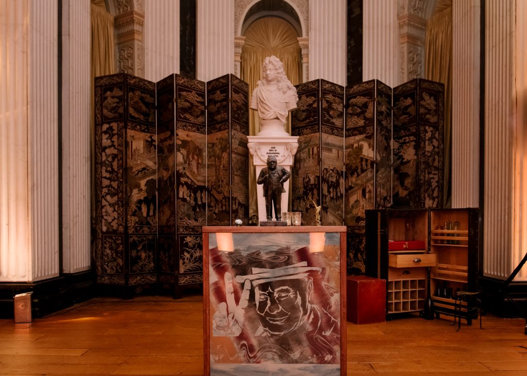 A bust of Winston Churchill on a wooden plinth with an etching of Winston Churchill and the famous Victory sign. Luxury event planner.