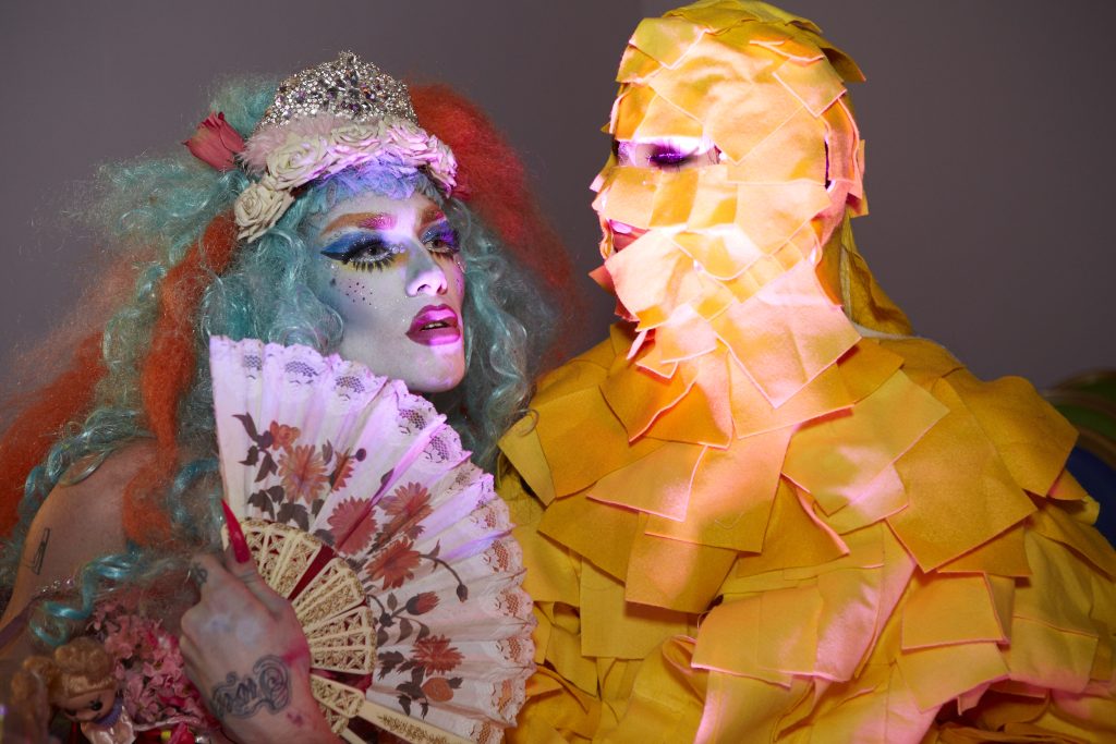 A drag queen and a mannequin covered in cheese slices.