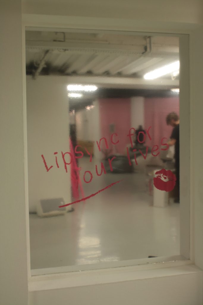 The words "Lipsync for your lives" vinyled onto a mirror window.