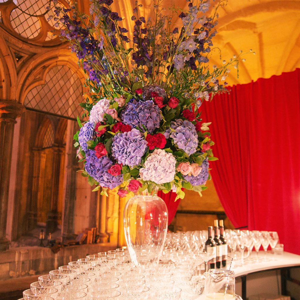 Flowers in a vase set on a bar in front of a red curtain.
