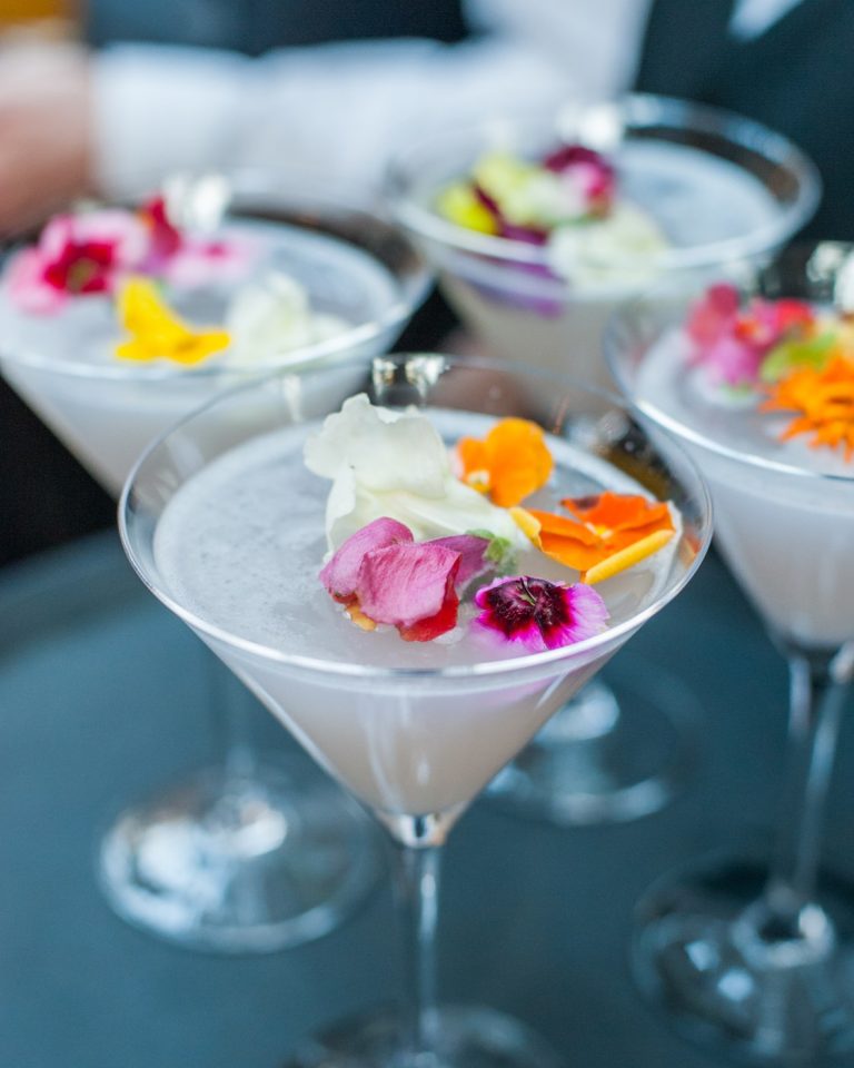 Martini glasses garnished with edible flowers and petals, shot close and shallow against a dark ground