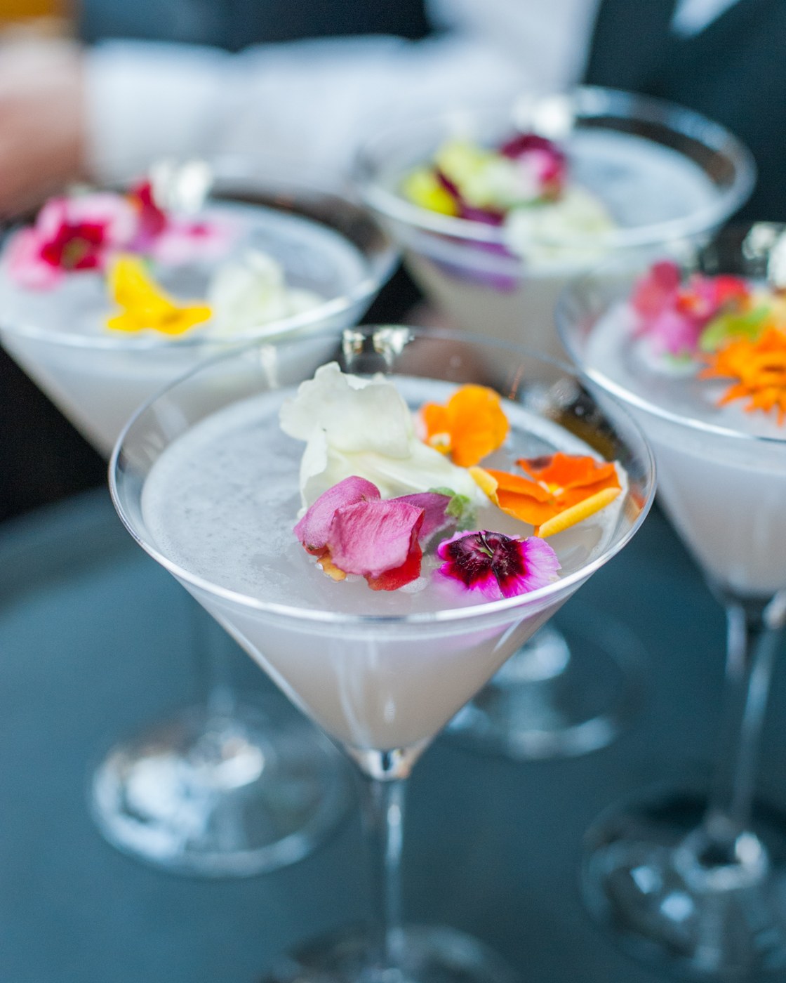 Martini glasses garnished with edible flowers and petals, shot close and shallow against a dark ground