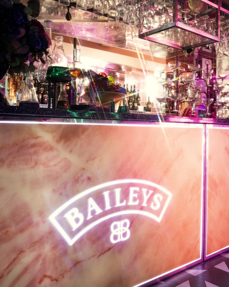 A bespoke marble bar unit with an illuminated Baileys logo and glassware racked overhead