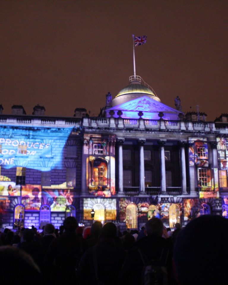 The full facade of Somerset House turned into a projection-mapped screen, with a crowd gathered on the lawn below