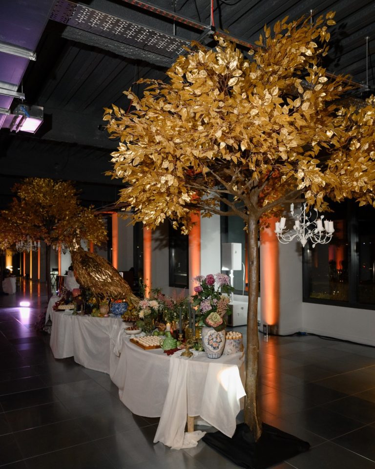 A themed banquet corridor with gilded trees, a golden peacock and a laden feast table under warm chandeliers