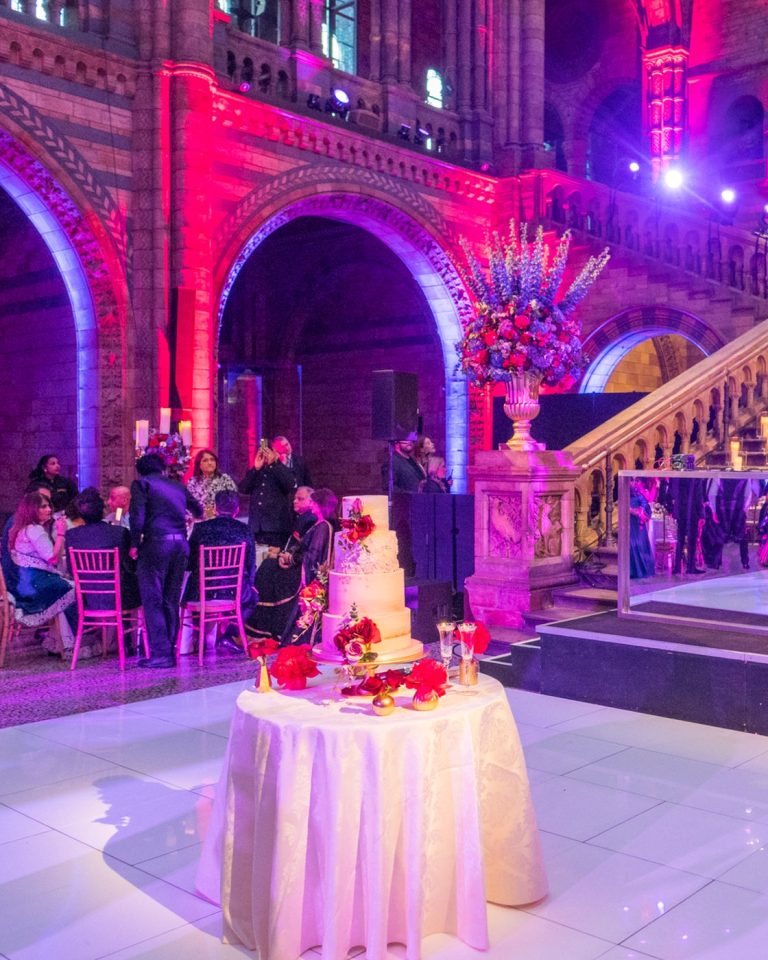 The Natural History Museum staircase dressed for a wedding reception with a cake table, washed in red and violet light