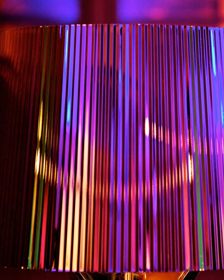 A close detail of a fringed glass lampshade glowing in shifting jewel colours against soft bokeh