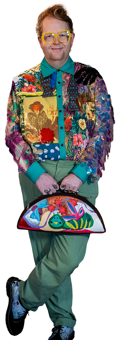 Christopher Mills standing in a patchwork jacket and sage trousers, holding a hand-painted case.