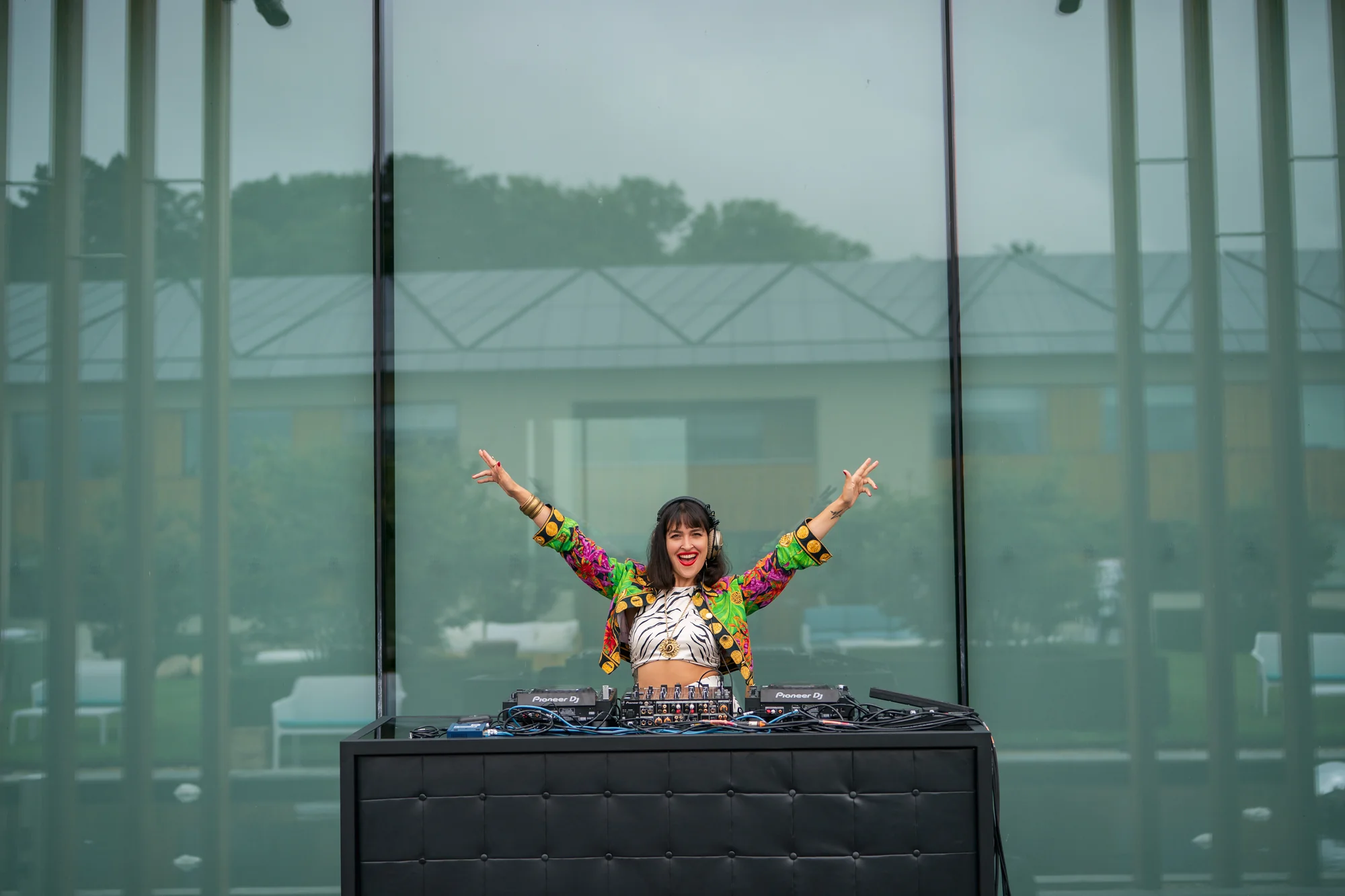 The DJ throwing both arms up behind the decks, the panoramic windows and the view beyond her.