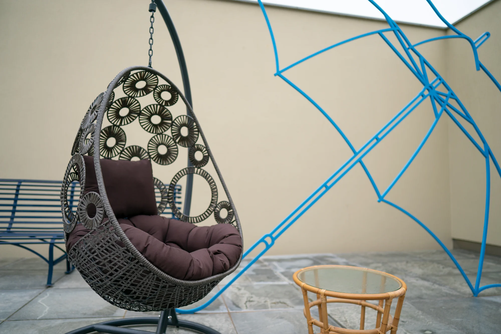 A hanging rattan chair on the patio beside a blue line sculpture set against the wall.