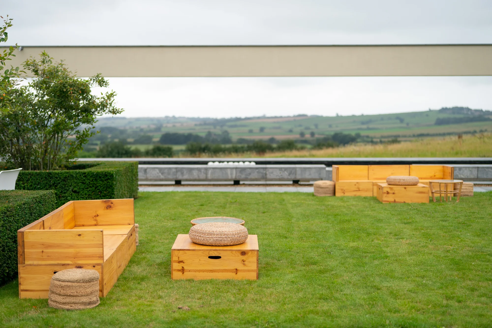 Timber crates and cushions set out on the lawn as low seating, the valley opening up beyond the parapet.