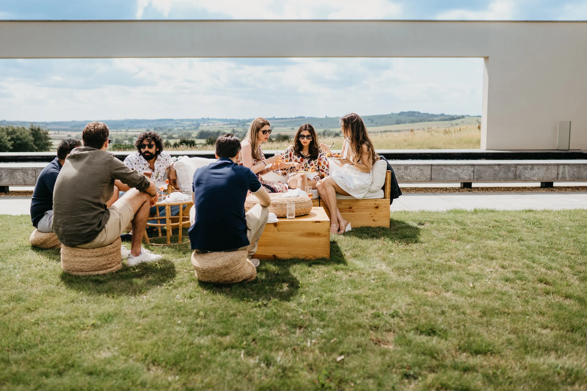 Guests sitting out on the lawn on low cushions and rattan seats, talking in the sun.