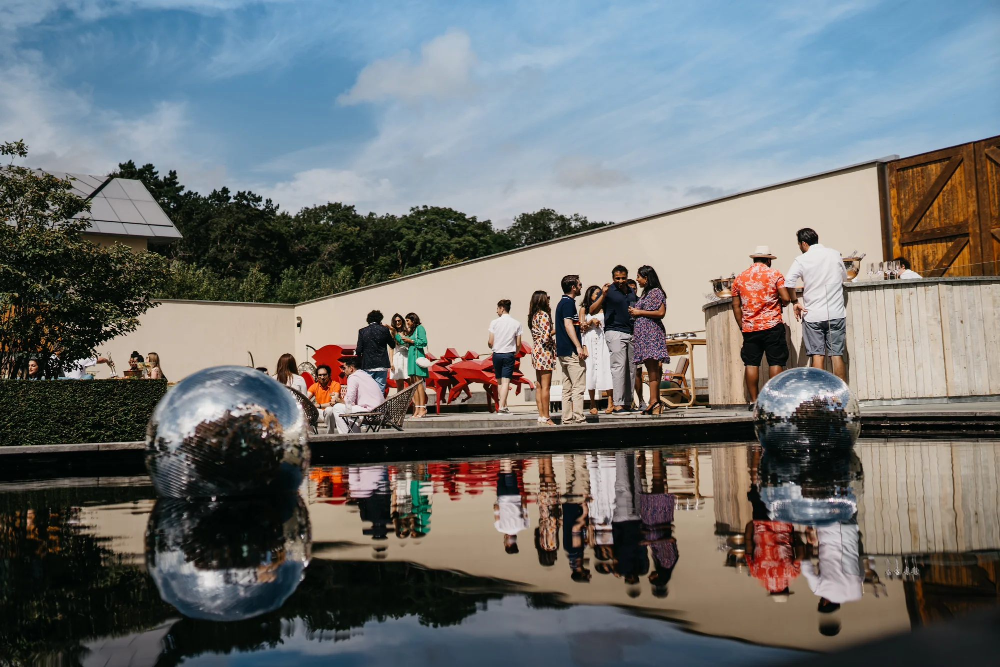 Guests gathered along both sides of the reflection pool in the afternoon sun, mirror balls on the water between them.