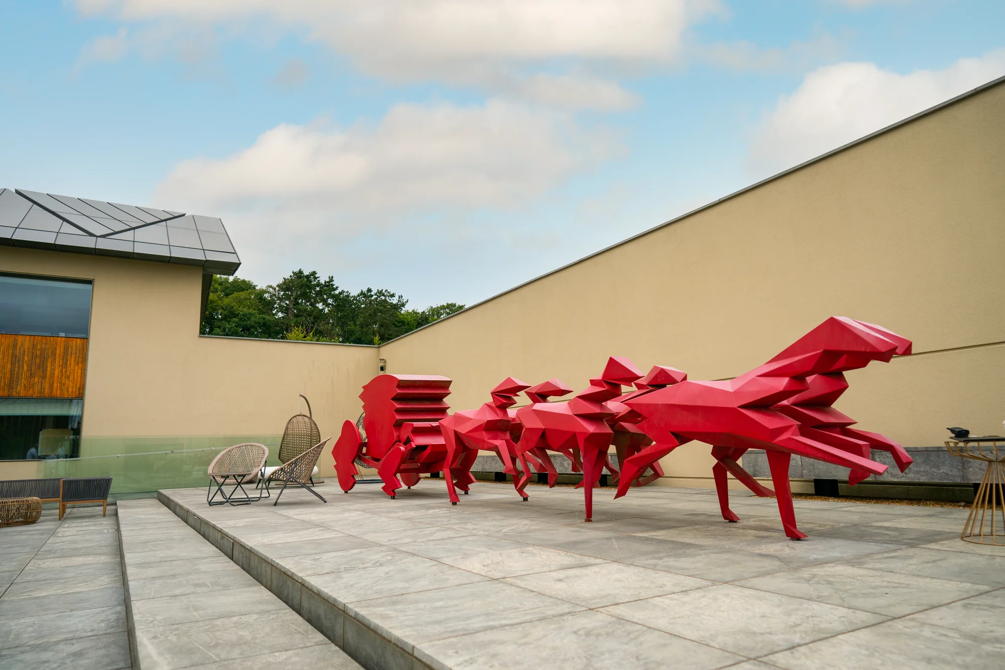 A large red sculpture on the paving outside the building, a speaker stack and seating set out beside it.