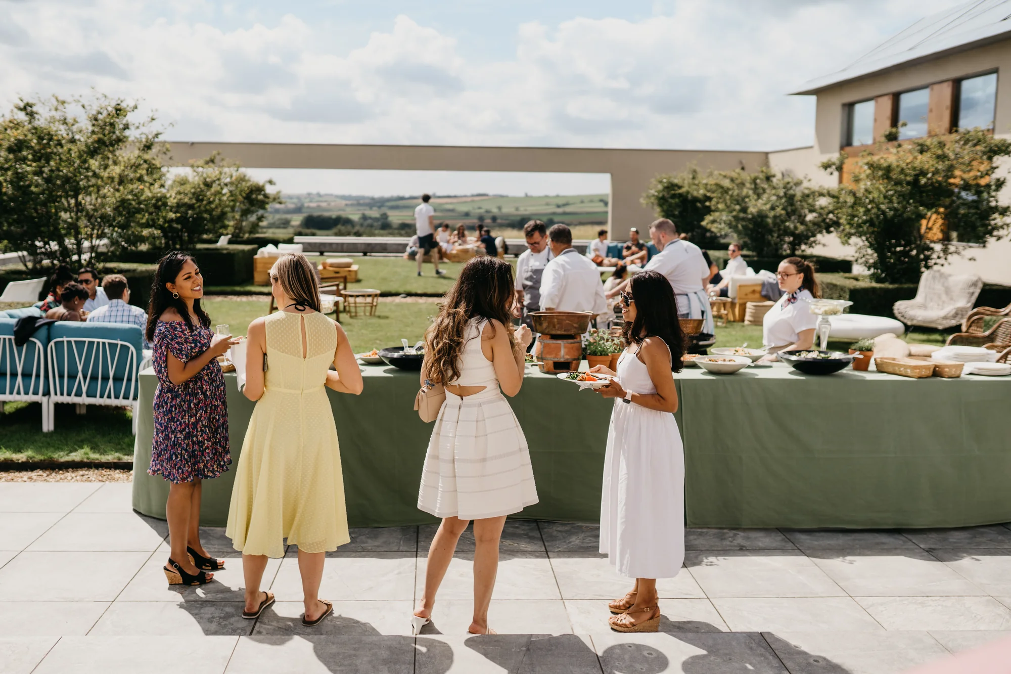 Guests standing at a circular bar built from recycled wood on the terrace, the gardens dropping away behind them.