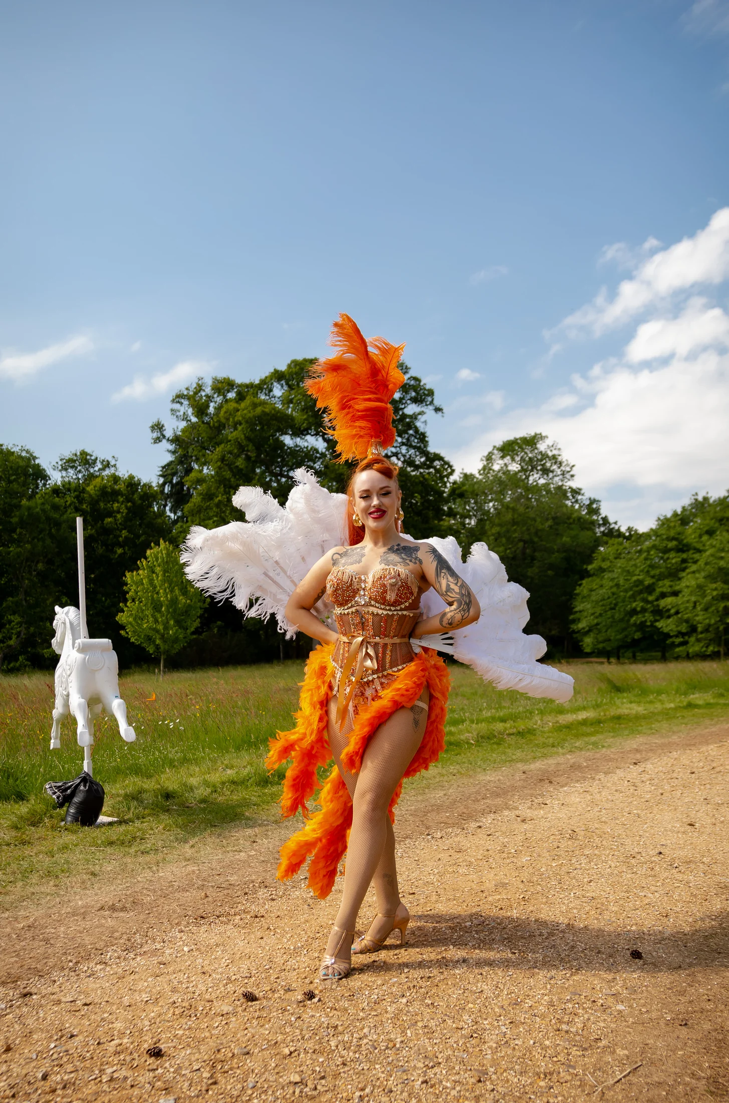 A dancer in orange and white feathers walking up the drive towards the house.