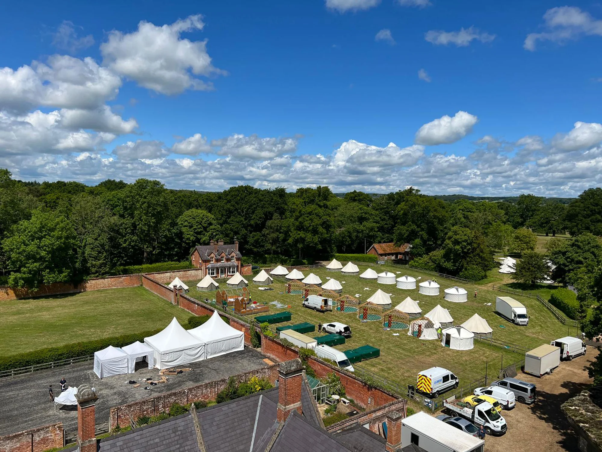 The glamping field from above, rows of bell tents pitched in the parkland beyond the house.