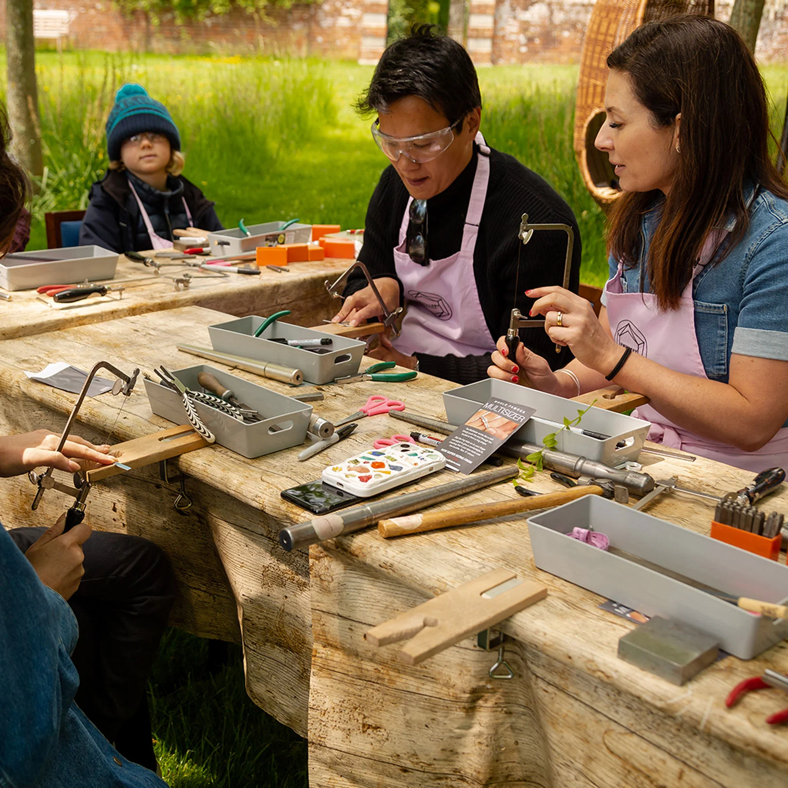 Guests at a timber workbench making jewellery, tools and findings laid out in trays.