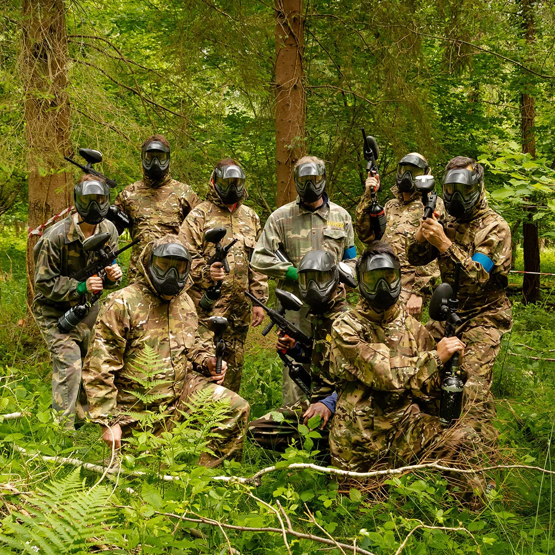A paintball team in camouflage and masks gathered among the ferns in the woodland.