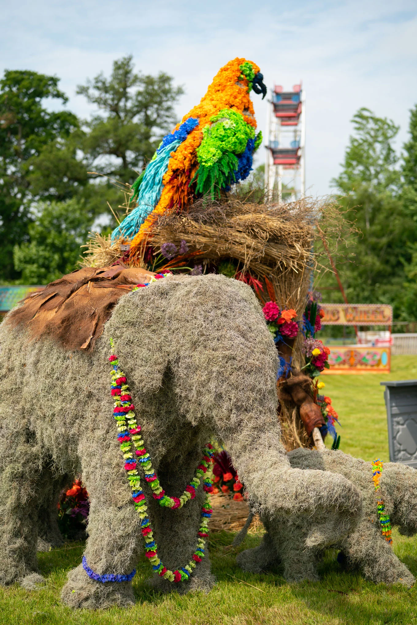 An elephant built from straw and foliage with a macaw on its back and a garland of flowers around its neck.