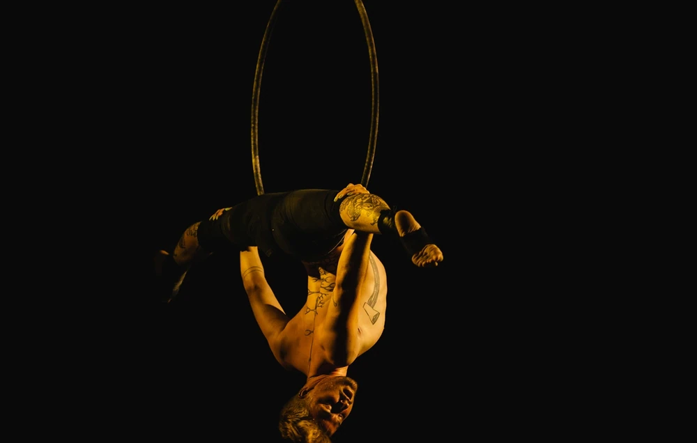 An aerialist suspended in a hoop above the hall, lit against black.