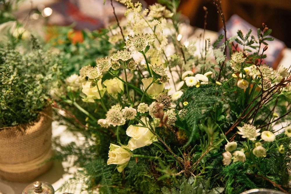 A close view of a centrepiece of white flowers, herbs and foliage in a hessian-wrapped pot.