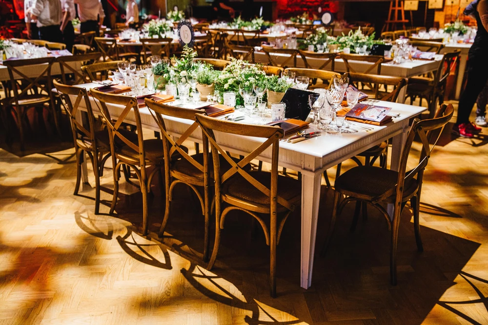 Long trestle tables dressed with greenery and glassware on the wooden floor of Jerwood Hall.
