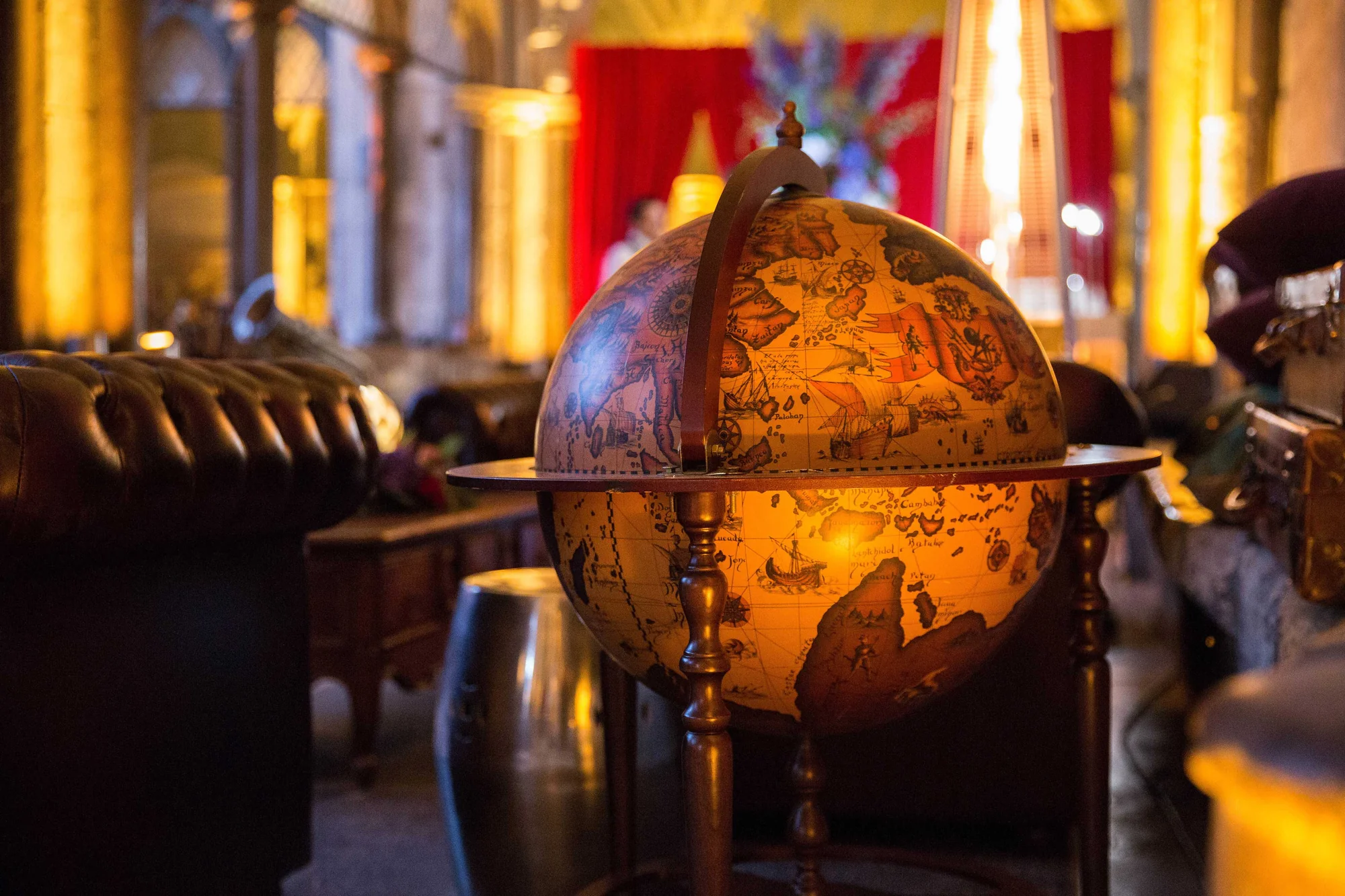 A lit antique globe on a stand in front of heavy red drapes, the stonework warm behind it.