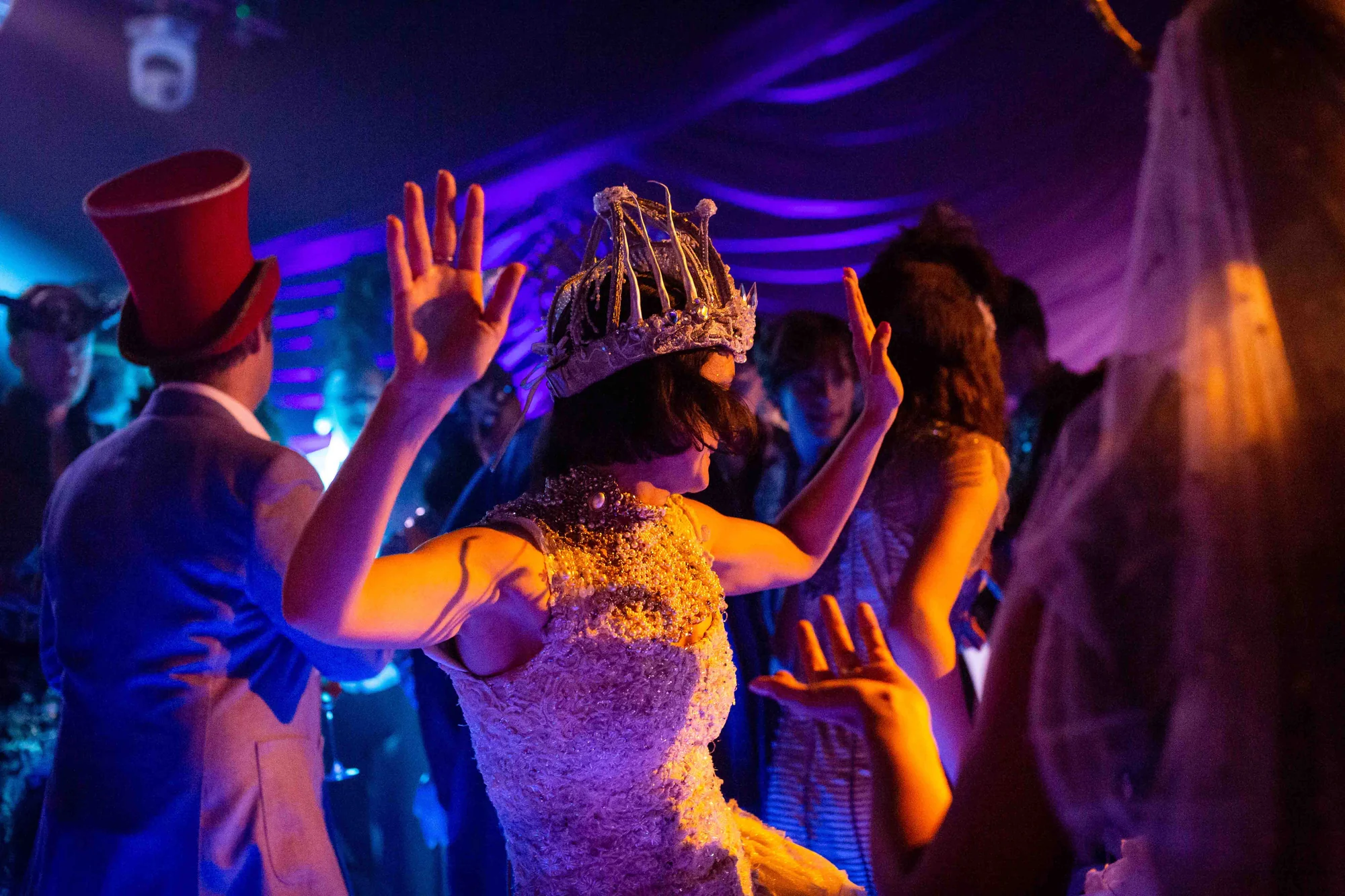Guests dancing under coloured light, a crown and a top hat among them.